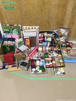 Overview of gift bags, gift boxes, and assorted spools of ribbons arranged on floor with wood paneling background.