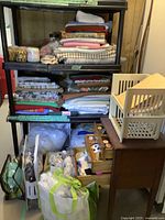 Overall shelf displaying folded fabric stacks, assorted sewing materials, yarn bags, fiber fill, and small wooden cabinet.