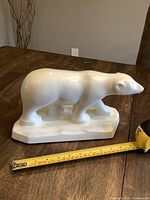 Side view of white ceramic polar bear showing walking stance, smooth glossy surface, placed on wooden table with tape measurement showing size approximately 11 inches in length.