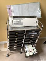 White Cricut Expression machine on chrome 14-drawer cart with cutting mat behind