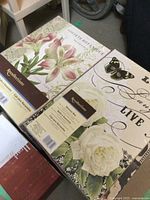 Top view of two cardboard memory boxes featuring lily flowers with pink tones, and white rose with butterfly and cursive text on lid.