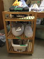 Wooden three-shelf trolley holding spa items including paraffin bath, plastic cups, foot bath, and foot massager on top shelf.