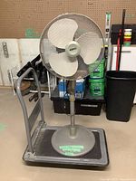 Floor fan on top of the hand truck showing fan blades, protective guard, and base.