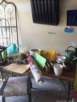 Table with assorted gardening pots, watering cans, burlap roll, kneeling cushion, and other gardening accessories