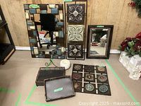 Photo showing two framed mirrors, white textured candle, metal wall art with circular designs, and two metal trays arranged on the floor.