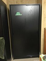 Front view of black IKEA wardrobe with both sliding doors closed, showing wood grain texture.