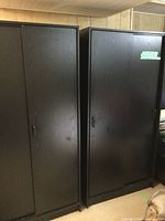 Two black IKEA wardrobe cabinets standing side by side with sliding doors closed.