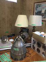 Two end table lamps with white shades, brass bases, and various ceiling fixtures on a wooden table in a basement room with wood paneling.