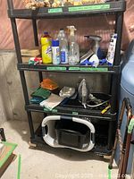 Full view of black shelving unit with cleaning supplies, steam cleaner, iron, cloths, and basket on bottom shelf
