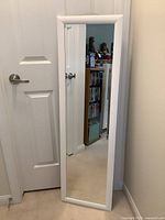 Full view of the white framed rectangular mirror placed against a wall near a door, showing its shape and frame.