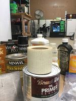 Photo showing cans and bottles of Minwax wood finishes, Beautiful Tone oil primer sealer opened, and other finishing products on a table in a workshop area.