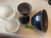 Five mixing/serving bowls arranged on a flat surface: two white bowls and three navy blue with grey inside bowls showing variety of sizes.