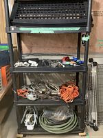 Full view of plastic shelving unit with various cords, chains, ratchet straps, and garden hose