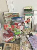 Photo showing a pile of scrapbooking and card making supplies including idea books, embossing powders, ribbons, paper cutters, stamps, and envelopes.