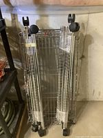 Two steel wire racks with multiple shelves and caster wheels, shown standing upright against a concrete wall.