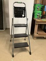 4-step metal ladder with black plastic steps and tool tray top, standing on basement floor.