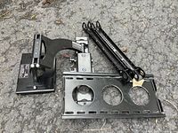 Top-down view of TV mount components showing articulating arm and mounting plates on asphalt ground.