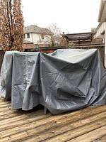 Gray vinyl cover placed over outdoor patio furniture sets on wooden deck, showing size and fit.