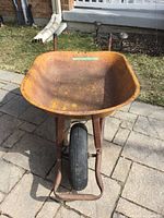 Front view of rusty metal tray and black inflated tire on wheelbarrow