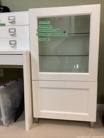 Front view of white cabinet showing closed glass door and chrome legs