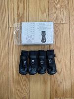 Photo of four black GF Pet Elasto-fit boots arranged in front of product packaging, laid on a wooden floor