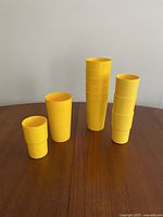 Photo showing the 10 yellow stackable drink cups: 4 short and 6 tall, arranged side by side on a flat surface.