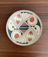 Top view of the round pottery plate showing the intricate black and red painted geometric and bird motifs.
