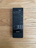 Top full view of a black Sony remote control RM-Y133 placed on wooden flooring showing all buttons and layout.