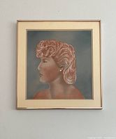 Front view of framed pastel portrait artwork showing profile of woman with styled hair on blue-gray background.