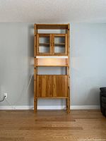 Front view of the full wall unit showing upper glass doors and lower wood cabinets on wooden frame with adjustable vertical supports.