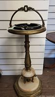 Full view of the antique ashtray stand showing the brass and alabaster construction with black glass ashtray insert and handle on top.