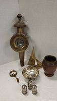 Antique brass car lamp, brass sailboat, copper vase, silver-toned pierced bowl, silver-toned pierced shakers, and brass lorgnette arranged on table.