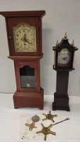 Two upright clocks side by side with clock repair wheels and keys in front, showing scale and included parts.