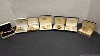 Full view of multiple sets of cufflinks and tie pins displayed in and out of boxes on black surface