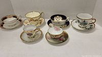All 5 vintage demitasse cups and matching saucers arranged in row showing different floral patterns and gold trims.