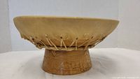 Side view of drum showing natural skin head and wooden base with string tensioning