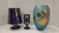 Set of three blue vases against a white background, showing their varying sizes and gold detailing.