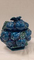 Front view of blue grape cookie jar with lid on, showing glossy grape and leaf detail