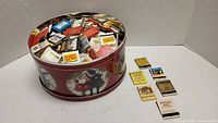 Large open tin filled with assorted vintage matchbooks, some loose outside the tin