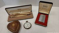 Overview photo showing all items: Waltham pocket watch, Swank lighter in box, two Cross pens in case, small heart-shaped leather box
