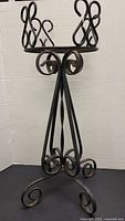 Full view of black metal iron plant stand with scroll legs and round top.