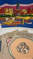 Close-up of kraft paper posters featuring stylized fruit smoothie illustrations labeled 'Cantaloupe Smoothie' and 'Strawberry Margarita'.