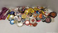 Top view of approx. 50 mixed vintage campaign and promotional buttons with various slogans, logos, and colors.