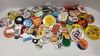 Photo showing a pile of approximately 50 assorted vintage campaign buttons with a variety of colorful graphics and text.