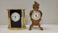 Front view of two clocks: an ornate gold-tone metal clock and a brass and black Seth Thomas clock.