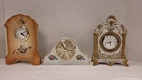 Front view of three porcelain mantle clocks showing varying styles and sizes.