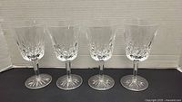 Set of 4 clear Waterford crystal wine glasses in a row showing cut pattern and starburst base.