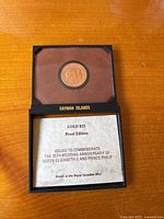 Open presentation box showing coin mounted in brown velvet interior above printed certificate insert