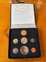 Seven coins in original black foam insert and white satin-lined keepsake box