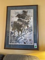 Full view of the framed print on wall showing wolves in snowy landscape with wooden frame and blue mat